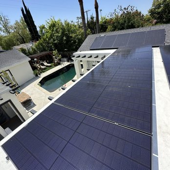 Neosun - The image shows multiple solar panels installed on a residential roof, with a backyard featuring a swimming pool, patio furniture, and surrounding trees. The sky is clear and blue, indicating sunny weather. Tall palm trees and other greenery are visible behind the house, emphasizing a suburban setting. The solar panels are aligned in rows, covering a significant portion of the roof, and are positioned to maximize sunlight exposure. - Solar Installation Near Me - Burbank, California