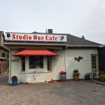 Studio One Cafe - Studio one cafe - Exterior view of Studio One Cafe with a red awning, potted plants, and a sign indicating it is open, located near residential buildings. - Breakfast & Brunch Near Me - Eugene, Oregon