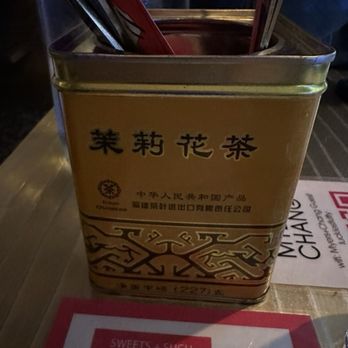 Myers & Chang - A metal container with Chinese characters and decorative patterns holds chopsticks and utensils on a table at a restaurant. - Asian Fusion Near Me - Boston, Massachusetts