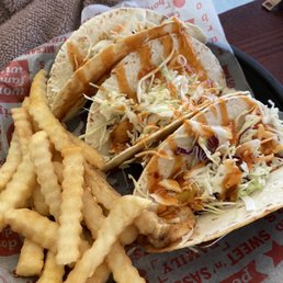 Buffalo Shrimp Tacos - Three tacos filled with shredded lettuce and sauce are placed on a tray with crinkle-cut French fries, served at a restaurant.