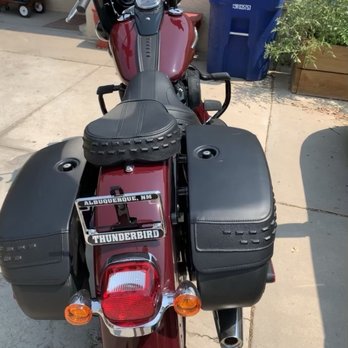 Thunderbird Harley-Davidson - Bike - A red Harley-Davidson motorcycle with black saddlebags and a seat is parked on a concrete surface, with a blue trash bin and greenery in the background. - Motorcycle Dealers Near Me - Albuquerque, New Mexico