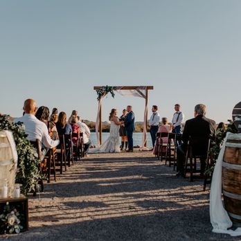Rustique Rentals - An outdoor wedding ceremony with guests seated on chairs, facing a couple exchanging vows under a wooden arch, with barrels and signs as decorations. - Party Equipment Rentals Near Me - Buckeye, Arizona