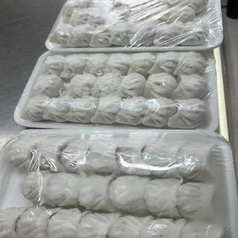 Dim Sum House - Har Gow Galore - Three foam trays filled with frozen dumplings, covered with plastic wrap, are placed on a stainless steel surface. - Dim Sum Near Me - Chicago, Illinois
