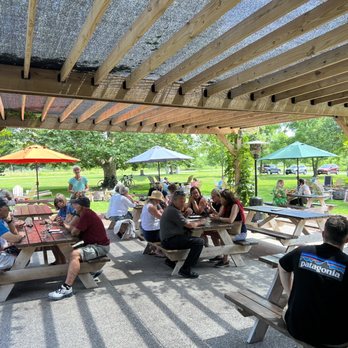 Brewery Ardennes - Outdoor space. Mix of picnic tables with umbrellas and Adirondack chairs around barrel tables - Breweries Near Me - Geneva, New York Brewery Ardennes - Outdoor space. Mix of picnic tables with umbrellas and Adirondack chairs around barrel tables - Breweries Near Me - Geneva, New York