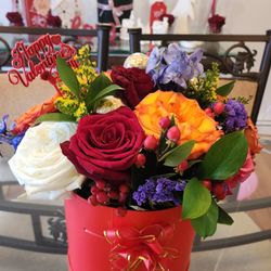 A beautiful red box adorned with a lavish gamut of roses and an array of colors that renders the arrangement...