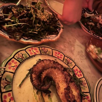 Bar Isabel - A fish fillet with a charred exterior is presented on a colorful, patterned plate with a creamy sauce and some greens. - Spanish Near Me - Toronto, Ontario