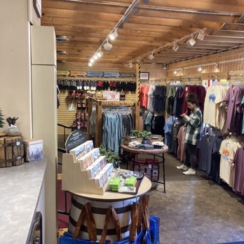 Brownfield's - Inside a retail clothing store, racks of shirts and jackets are displayed, with a customer browsing and using her phone. - Outdoor Gear Near Me - Estes Park, Colorado