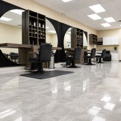 Elegant Barber Shop - Wide view of the barber stations, round mirrors, black chairs, and polished tile floors.