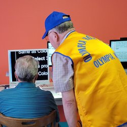 Lions Low Vision Center - Man in lion's vest assisting low vision client at reading machine