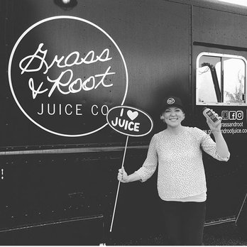 Grass & Root Juice Co - a woman holding a sign - Juice Bars & Smoothies Near Me