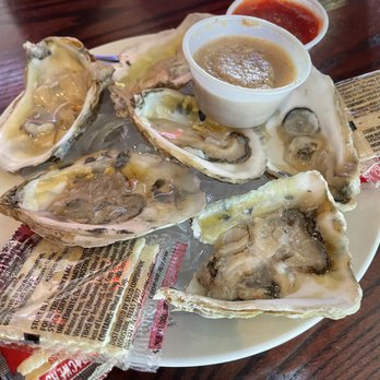 Jefferson's - Half dozen raw oysters - Six raw oysters on the half shell are presented on a white plate, accompanied by small cups of cocktail sauce and mignonette, with a lemon wedge in the background. - American Near Me - Lawrence, Kansas