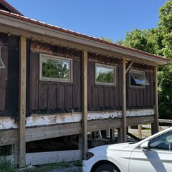 Dilapidated siding and garbage thrown under the building, including bar stools and big strips of insulation.