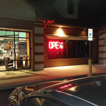 21st Amendment - a car parked in front of a restaurant - A brick storefront features a bright red neon 'OPEN' sign in the window, with interior lighting visible through the glass door and window. - Beer, Wine & Spirits Near Me - Carmel, Indiana