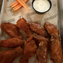 Wednesday wing special - A metal tray contains several buffalo chicken wings coated in sauce, accompanied by three celery sticks and a small cup of creamy dipping sauce, likely ranch or blue cheese. The tray is lined with branded paper from Pilot Project Brewing, Milwaukee, WI.