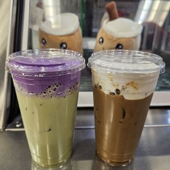 Yin Yang Tea - Matcha ube drink and salted Vietnamese coffee - Two iced beverages, one with purple and green layers and the other with brown and white layers, sit on a counter in front of a glass display with plush toy decorations. - Bubble Tea Near Me - Pasadena, California