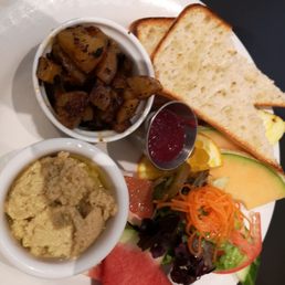 Vegan brunch plate with small salad, breakfast potatoes, housemade jam, toast and hummus and delicious fresh fruits