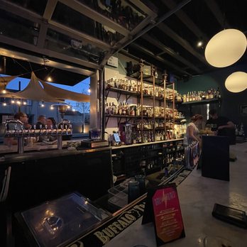 Dirty Laundry - a bar with a lot of bottles of alcohol - A bar interior with shelves stocked with liquor bottles, dim lighting, and patrons seated at the counter, with outdoor seating visible through the window. - Cocktail Bars Near Me - Denver, Colorado