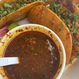a bowl of salsa and a plate of meat tacos