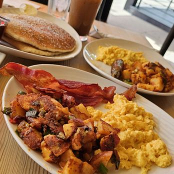 Jumpin Java - 2 breakfasts of scrambled eggs & breakfast potatoes, 1 with bacon, 1 sausage, & an order of pancakes. iced mocha in the background - Breakfast & Brunch Near Me - Studio City, California
