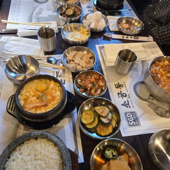 Sgd Dubu - A dining table with multiple small bowls of Korean side dishes, a bowl of rice, and hot pots, with chopsticks and utensils, at a Korean BBQ restaurant. - Korean Near Me - Madison, Wisconsin