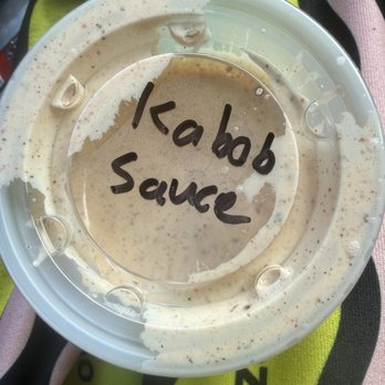 WhataKabob - A plastic bowl contains kabob sauce with a handwritten label on a transparent lid, placed on a colorful fabric surface. - Persian/Iranian Near Me - Austin, Texas