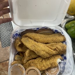 My food - A white takeout container holds fried fish fillets, potato wedges, and three small containers of dipping sauces, with a checkered paper lining.