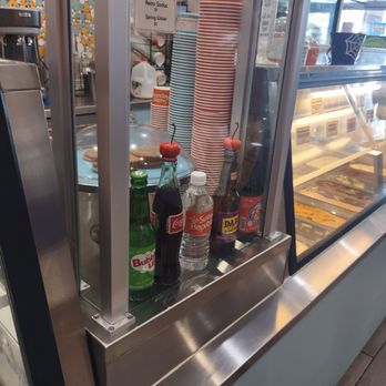 Sweet Republic - Bottled beverages - Various bottled drinks, including soda and water, are arranged behind a glass display at an ice cream shop, with paper cups and ice cream flavors visible nearby. - Ice Cream & Frozen Yogurt Near Me - Phoenix, Arizona