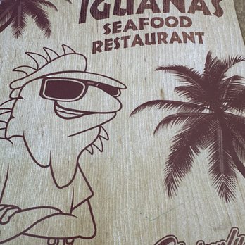 Iguanas - The menu cover displays a cartoon fish with sunglasses and crossed arms, alongside palm trees, representing a seafood restaurant with a tropical theme. - Seafood Near Me - St. Simons, Georgia