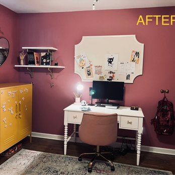 Handy Gus - Done! Cleaned up / patched walls / everything is sturdy! Added some hooks. A much neater look. - The room has a pink wall with a white desk positioned against it, holding a computer monitor, a lamp, and office supplies. A pink upholstered chair is in front of the desk. To the left, a yellow cabinet with magnetic letters and a stack of books is visible. Above the desk, a whiteboard with various drawings and notes is mounted, and two white shelves hold books and decorative items. A backpack hangs on the right side of the wall, and a patterned rug covers part of the dark wood floor. The image is labeled 'AFTER' in yellow text at the top right corner. - Handyman Near Me - Ridgefield Park, New Jersey