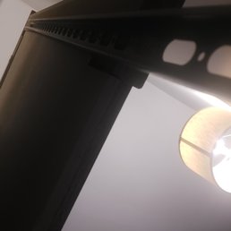The side of mirror propped up against wall - The image shows a black electronic device, likely a monitor or TV, viewed from below with a focus on its side and top edge, with a ceiling light in the background.