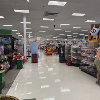 Target - The image shows a woman with gray hair, wearing a peach-colored shirt, beige shorts, and sneakers, browsing toys on a shelf in Target, Arlington Heights, IL. The store has bright lighting, a clean floor, and various toy displays, including a Target-themed dog figure on top of the shelves. The background features more aisles and shopping carts. - Department Stores Near Me - Arlington Heights, Illinois