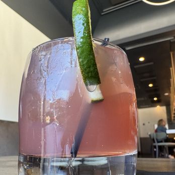 Modern Plate - Can't remember what the name was! - A pink-colored cocktail in a clear glass with a lime wedge garnish, placed on a table inside a restaurant with dark ceiling and lighting fixtures. - Cocktail Bars Near Me - Elmhurst, Illinois