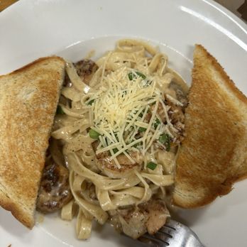 Cormier’s Kitchen - Shrimp Pasta - Shrimp pasta with creamy sauce, shredded cheese, and green onions, accompanied by two slices of toasted bread on a white plate. - Southern Near Me - Spring, Texas