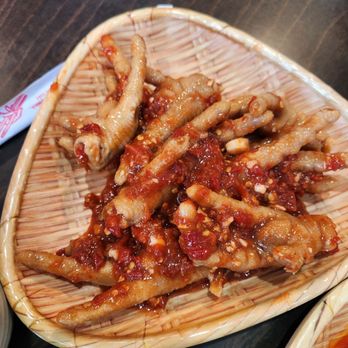 Noodle's Time - Chicken feet - Chicken feet coated in a red, spicy sauce are presented in a woven bamboo basket, placed on a dark wooden table. The dish is a traditional Chinese appetizer, featuring tender chicken feet with a flavorful, spicy sauce. The basket's natural texture contrasts with the vibrant color of the sauce, highlighting the dish's presentation. - Chinese Near Me - Edison, New Jersey