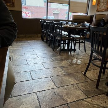 Al-Ameer - A restaurant interior featuring a large window with blinds, wooden tables set for dining, and black chairs with cushioned seats. - Middle Eastern Near Me - Dearborn, Michigan