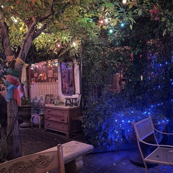 Glai Baan - outdoor space - A nighttime outdoor space features a tree with colorful string lights, surrounded by bushes with blue lights, and outdoor furniture including chairs and a table. - Thai Near Me - Phoenix, Arizona