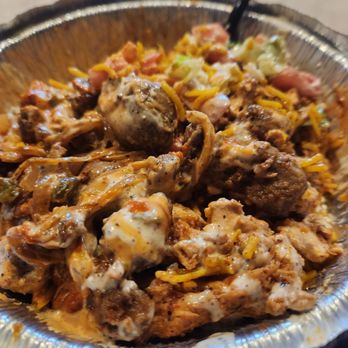 Buns On Fire - A foil container holds a mixture of cooked meat, melted cheese, and vegetables, with a black fork inserted into the food. - Juice Bars & Smoothies Near Me - Buffalo Grove, Illinois
