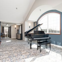 Vista Prairie at Copperleaf - Located on the second-floor balcony, this lounge features a polished black baby grand piano set against a large arched window...