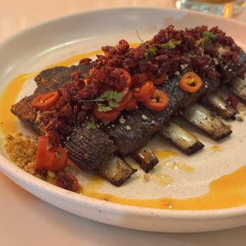 Eyval - Lamb ribs - Grilled lamb ribs with chili, herbs, and spices served on a white plate, with sauce drizzled around. - Persian/Iranian Near Me - Brooklyn, New York