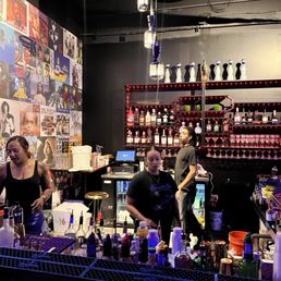 Bar area in spin room - A bar scene at Spin Room in Phoenix, AZ, featuring three bartenders behind the counter with liquor bottles and bar tools, and a wall decorated with music album covers.