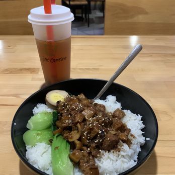 Light Cantine - Pork belly rice bowl - A meal featuring rice topped with pork and vegetables, accompanied by iced tea in a to-go cup, on a wooden table in a casual restaurant setting. - Bubble Tea Near Me - Madison Heights, Michigan