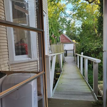 Caroline's Table - Walk up to patio - A wooden outdoor ramp extends from a building, bordered by white railings, with trees and a house visible in the background. - New American Near Me - Denton, Maryland