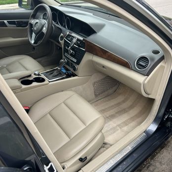 niko's detailing spa - The image shows the interior of a Mercedes-Benz vehicle with beige leather seats and matching beige carpeting. The dashboard includes wood trim accents, a central control panel with various buttons, and a mounted phone holder. The steering wheel has the Mercedes-Benz logo, and the front passenger seat is visible. The interior appears clean and well-maintained, with a view of the outside street through the window. - Auto Detailing Near Me - Chicago, Illinois