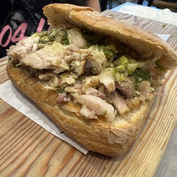 Meat & Bread - Porchetta Sandwich - A sandwich filled with roasted pork, crispy crackling, and green herbs, served in a bread roll on a wooden board. - Sandwiches Near Me - Austin, Texas