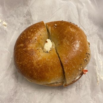 Bagelry - a half eaten bagel with butter - A bagel with a shiny, golden-brown crust, topped with sesame and poppy seeds, partially sliced open with cream cheese visible inside. - Bagels Near Me - Cedarhurst, New York