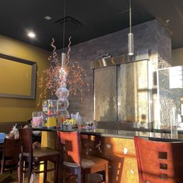 A restaurant interior featuring a bar with high chairs, a decorative light fixture, and a stone wall behind the bar area.