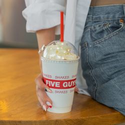 Five Guys - A close-up photograph of a woman holding a Five Guys milkshake.