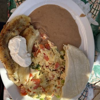 Tune-Up Cafe - Huevos el salvadoreño. Scramble with plantain and beans - A breakfast plate includes scrambled eggs mixed with diced tomatoes and green peppers, fried plantains topped with sour cream, refried beans, and a folded tortilla. The dish is served on a white plate placed on a table with a patterned tablecloth. The meal showcases Salvadoran cuisine with a variety of textures and flavors. - New Mexican Cuisine Near Me - Santa Fe, New Mexico