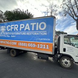 CFR Patio truck wrap - A medium-sized delivery truck displays a large, colorful advertisement for CFR Patio, an outdoor furniture restoration business. The ad includes the company name, website, phone number, and social media handle, with a tagline about outdoor furniture. The truck is parked in an outdoor lot with trees and other vehicles visible in the background. The truck's cab is white with business details printed on the door.