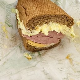 Salad With Egg Salad - A sandwich with ham, cheese, egg salad, and lettuce on whole wheat bread, partially eaten, on a paper wrapper.